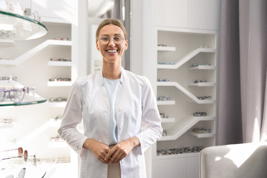Portrait adult female ophthalmologist in uniform standing in optician store, posing for camera, represents expertise in vision care, eye health consultation, optical service, qualified medical support