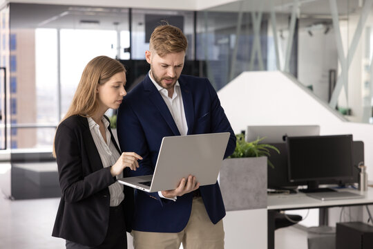 Two diverse businesspeople creative professionals colleagues reviewing digital data on laptop in modern open space office cooperating on task planning and problem solving brainstorming ideas as team