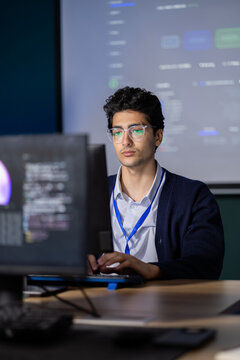 Software Developer sits beside desktop monitor within office workspace, considering computer software information during independent computer work, supporting practical technology skills.