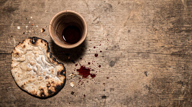 Communion Elements: A rustic wooden table bears the symbolic elements of communion &ndash; unleavened bread and a chalice of wine, with a few drops spilled.