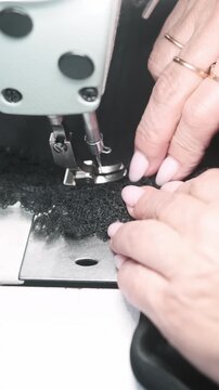Vertical video. Clothing production. Sewing lace. Dressmaker hand attaching garnish to black fabric corset. Manufacturing industry professional equipment.