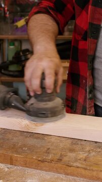 Vertical video. Carpentry process. Lumber work. Joiner polishing plank with professional orbital sander. Handyman occupation project workshop.