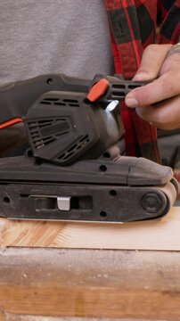 Vertical video. Woodworking process. Lumber equipment. Man polishing plank with handheld belt sander. Carpenter occupation with diy project workshop.