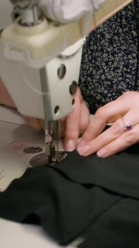 Vertical video. Clothing making. Sewing process. Seamstress hand working on stitching professional machine. Woman creating accurate seam on black fabric.