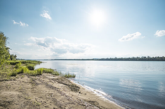 A wide steppe river in Kazakhstan, with aquatic plants drifting in the water under bright sunlight; a habitat rich in flora and fauna. A landscape suitable for use as a background