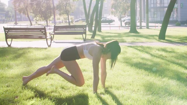 Active lifestyle. Urban workout. Woman doing physical exercise practicing yoga performing sportive fitness in sunlit green park.