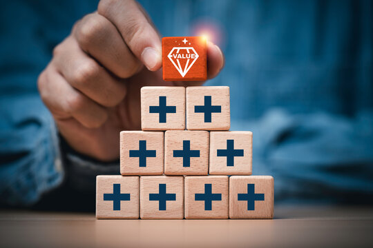 Hand placing a value diamond symbol on stacked wooden blocks with plus signs representing business value added , customer growth benefits creation and competitive advantage.