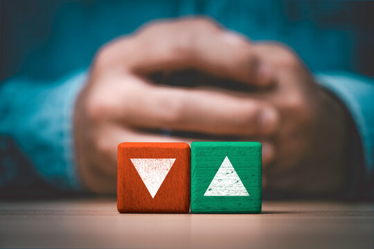 Red downward and green upward arrows on wooden blocks with hands in background symbolizing business growth and decline, financial risk of investment market trends and economic fluctuations.