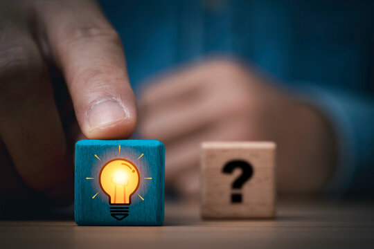 Creative problem solving and innovation concept with finger pushing a glowing light bulb icon on wooden block in front of a question mark symbolizing for new ideas inspiration and smart solutions.