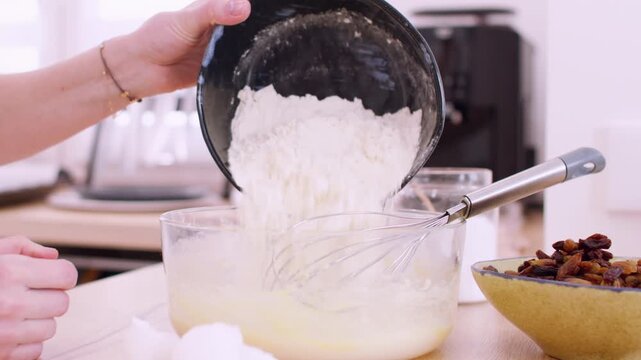 Baking process. Adding flour. Woman chef hand pouring white culinary powder in glass bowl whisk cooking dough pastry raisins meal.