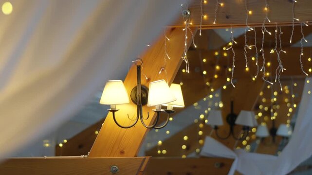Warm string lights and wall lamps illuminate draped fabric and wooden beams at a wedding venue