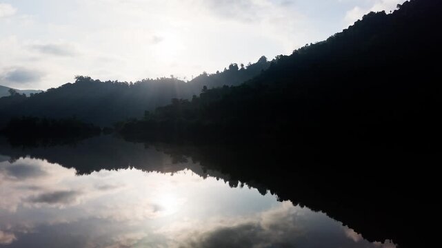 People explore the Da Lay Irrigation Reservoir in Lam Dong, Vietnam. The sun shines on the water and reflections appear on the lake. Nature surrounds this spot as clouds drift above.