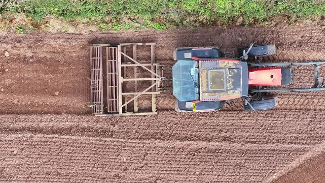 Top down aerial drone shot of a tractor cultivating dark soil in an agricultural field near Dalston with parallel tire tracks and freshly worked earth forming textured rows