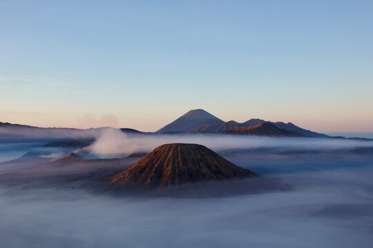 Aerial view of Mount Batok and Mount Bromo volcanoes rising above morning fog at sunrise with Semeru in the distance, Tengger caldera, East Java, Indonesia