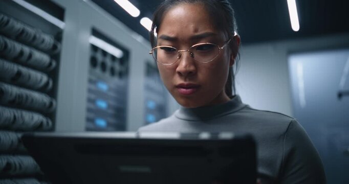 Female IT Technician Analyzes Information on Tablet Inside Modern Server Room. Concerned Expression Conveys Infrastructure Monitoring, Technical Troubleshooting and Digital System Reliability.