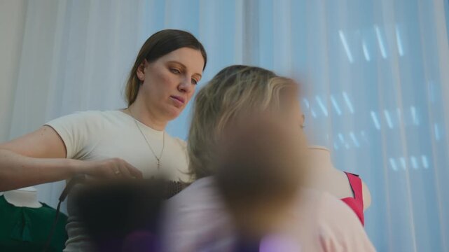 Stylist carefully uses a hairdryer on a client's hair. The stylist focuses intently on styling, showing concentration. The client sits patiently, trusting the stylist's skill