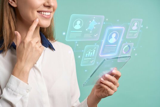 Smiling businesswoman touching chin while viewing futuristic holographic candidate profiles on transparent glass tablet, recruitment and talent management concept, mint green background