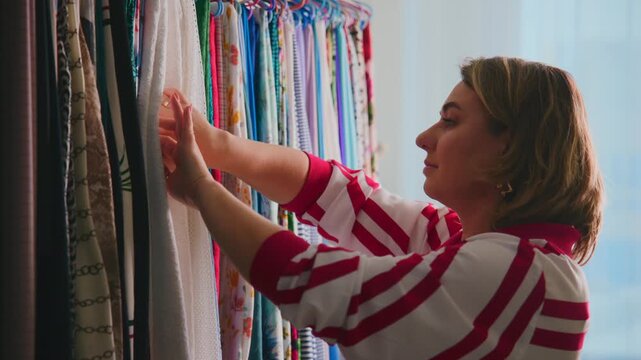 Woman touches fabric samples in bright, colorful textile store. She focuses closely, choosing material with care and interest. Scene captures calm, thoughtful shopping experience