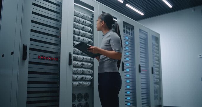 Worker Reviews Network Equipment and Cable Connections With Tablet in Server Facility. Modern Infrastructure Scene Conveys Preventive Maintenance, Technical Auditing, Connectivity, Digital Resilience.