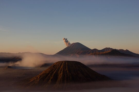 Sunrise over Mount Batok and Bromo volcanoes with erupting Mount Semeru releasing ash cloud above morning fog, Tengger caldera, East Java, Indonesia