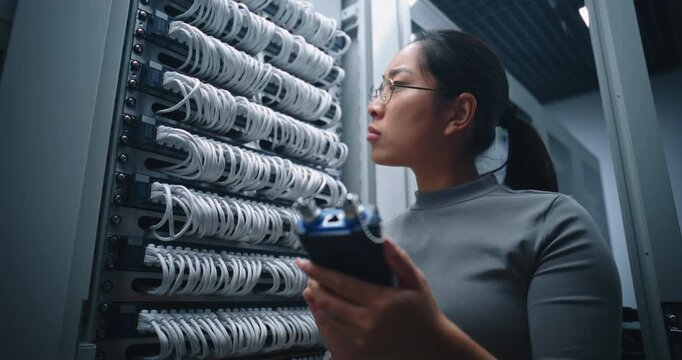 Female Engineer Diagnoses Ethernet Line Using Handheld Cable Tester in Server Room. Technical Scene Illustrates Connectivity Troubleshooting, Wiring Verification and Reliable Network Infrastructure.