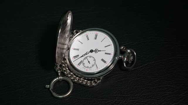 Time lapse of a vintage silver pocket watch with chain on black leather, hands moving from 2 to 3 AM during the daylight saving time change, forward and backward