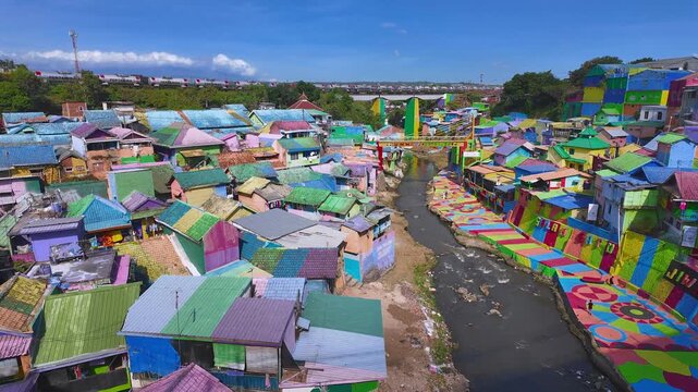 Elevated view of Jodipan Colorful Village, known as Kampung Warna-Warni, a tourism destination with colorful houses and urban art, as a freight train passes in the background. East Java, Indonesia.