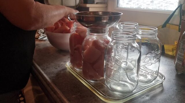 Female hands preparing fresh chicken in storage jars for household canning preservation
