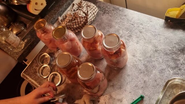 Female hands adding lid to glass mason jars with fresh chicken ready for canning storage