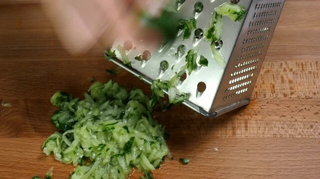 Cook grates a fresh cucumber. Green cucumber is ground on a grater to cook the dish.
