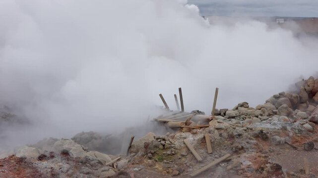 Thick steam billowing from the Gunnuhver geothermal vent over broken wooden boardwalk remains and altered clay, Reykjanes peninsula, Iceland, static shot