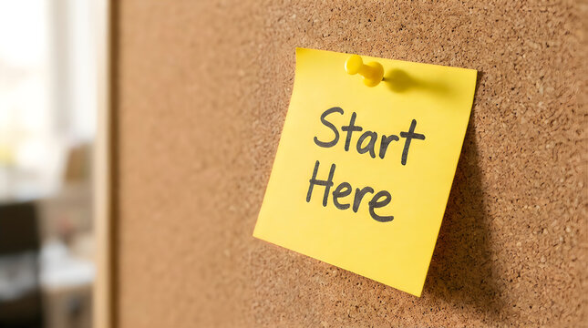 Yellow sticky note with Start Here text pinned to a cork board