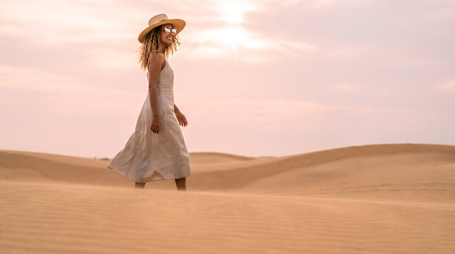 Woman in flowing linen dress standing in desert dunes at golden hour