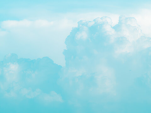 Soft pastel aqua blue sky with fluffy faded cumulus clouds and a tiny distant airplane, dreamy airy minimalist cloudscape background