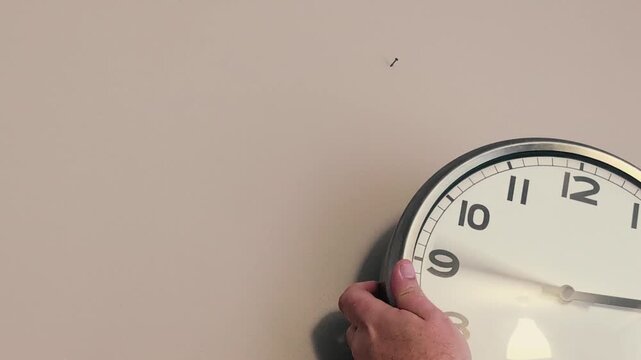 Hands set a wall clock back one hour for the change to winter time