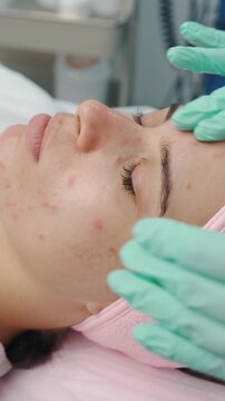 closeup of esthetician wearing green gloves gently applying serum to young woman's face during facial skincare