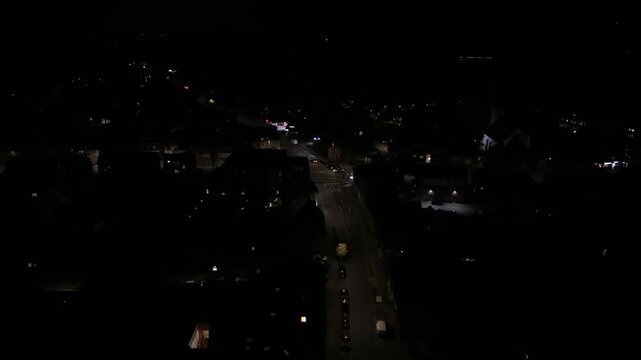 Driving cars on main street of small town at night. American housing area with warm lighting streetlights. Aerial dolly shot. Row of houses in historic city. Junction with glowing lanterns in autumn.