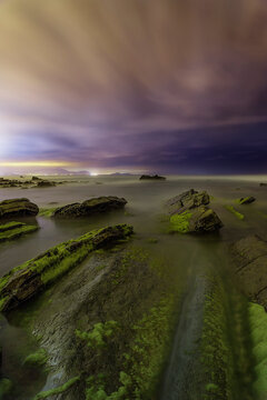 Night landscape of Barrika beach flysch rock formations under a dark blue starry sky and ocean waves in Biscay Basque Country Spain