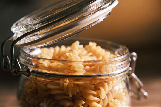 Open clip top glass jar filled with dry fusilli pasta on a dark wooden table