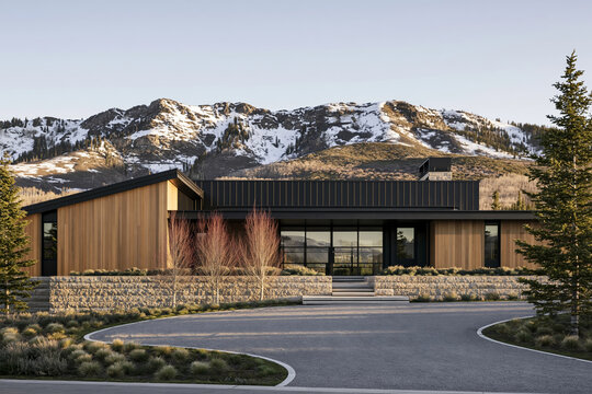 Mountain Modern house featuring golden cedar siding and matte black metal panels with snow-capped peaks in the background and a curved gravel driveway