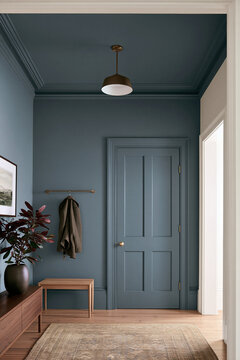 Mudroom corner with dusty stone blue walls, oak console, and wool jacket hanging on coat rack