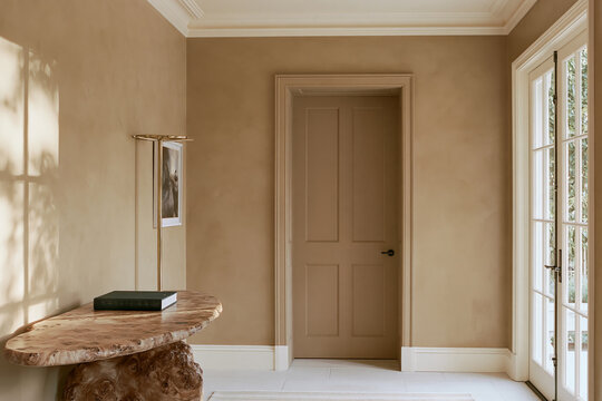 Entryway with sculptural burl wood console and brass coat rack in warm beige tones