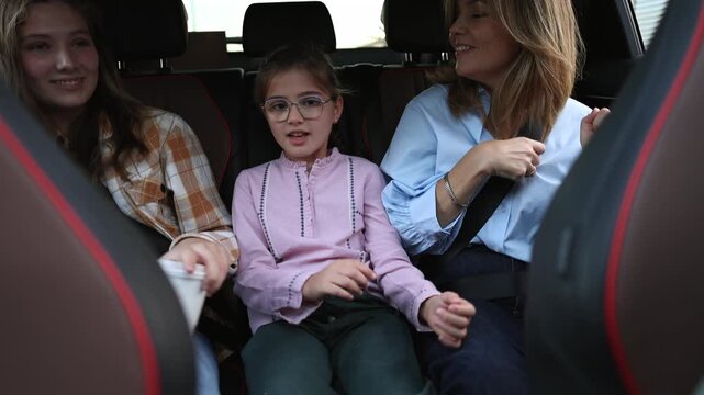 Joyful mother and two daughters dancing and singing along to music together in the backseat of a modern car, enjoying a carefree family road trip with smiles and laughter
