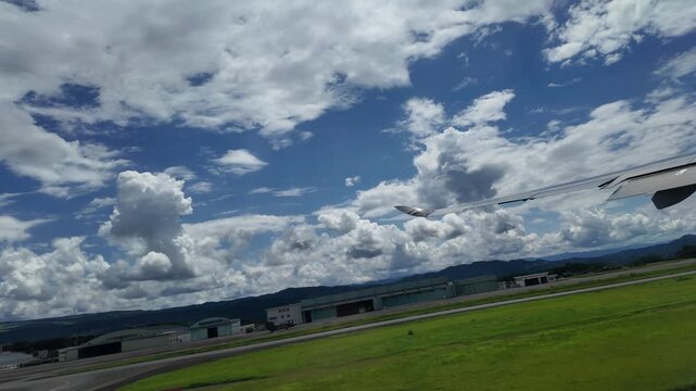 An airplane wing soars above green hills under dramatic cloudy skies.