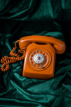 Bright orange vintage rotary phone on green velvet