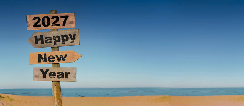 2027 happy new year written on a direction sign in front of a beach on blue sky