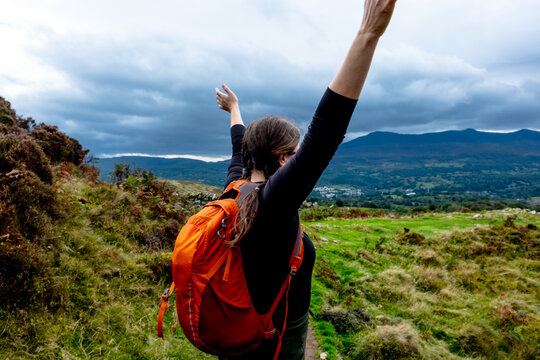 Woman with arms raised high celebrating on a mountain trail
