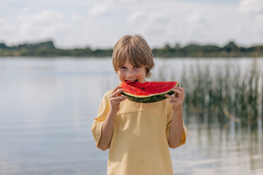 Happy young boy eating a juicy slice of watermelon outdoors