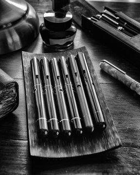 Set of luxury colorful acrylic fountain pens next to a vintage pocket watch and leather notebook on a wooden desk.