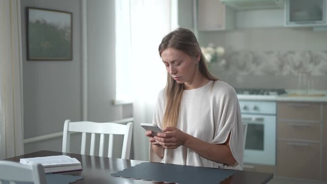 Young woman sitting at a table scrolling on her smartphone, thinking carefully before looking up with a sudden realization